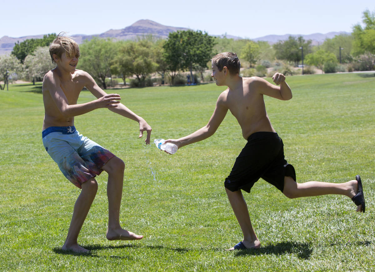 Chaz Henry, 14, runs away as Levi Henry, 12, splashes water on him at Exploration Peak Park on ...