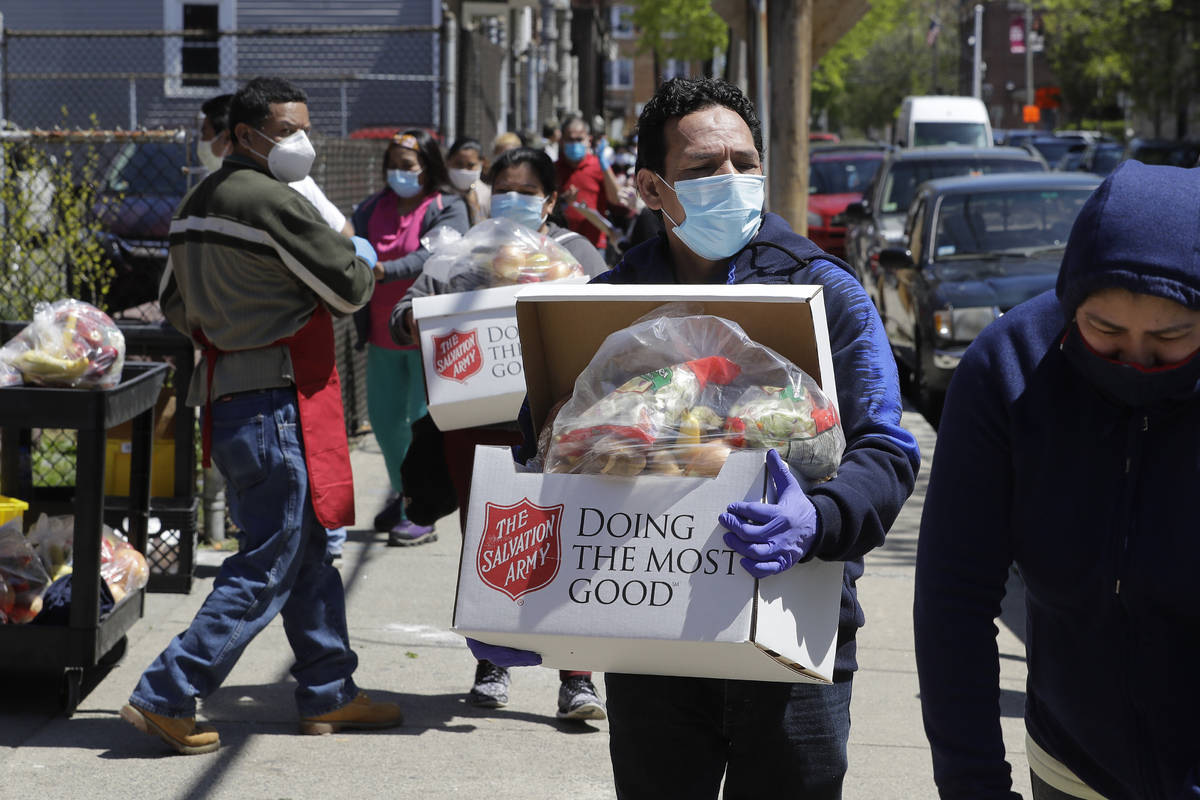 People wear masks out of concern for the coronavirus as they carry boxes of food they received ...