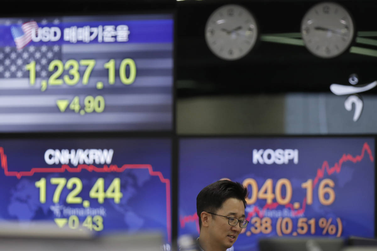 A currency trader talks near the screens showing the Korea Composite Stock Price Index (KOSPI), ...
