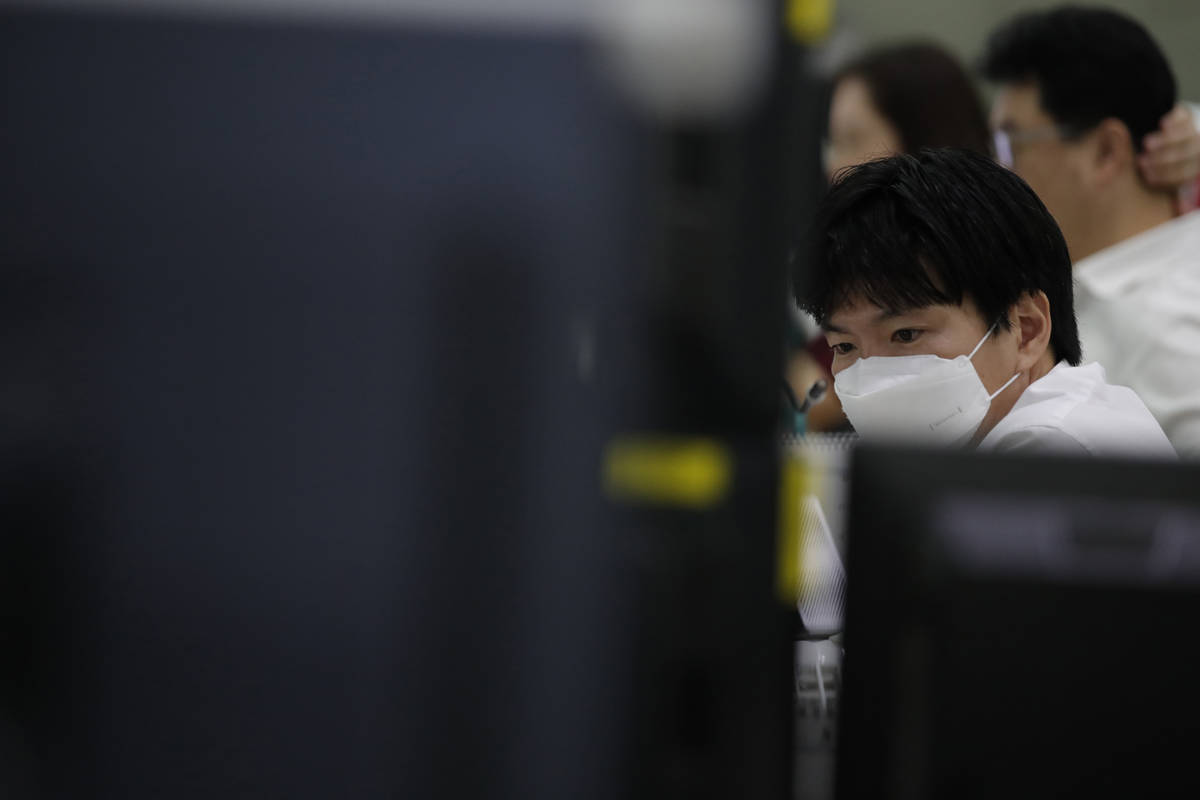 A currency trader wearing a face mask watches computer monitors at the foreign exchange dealing ...