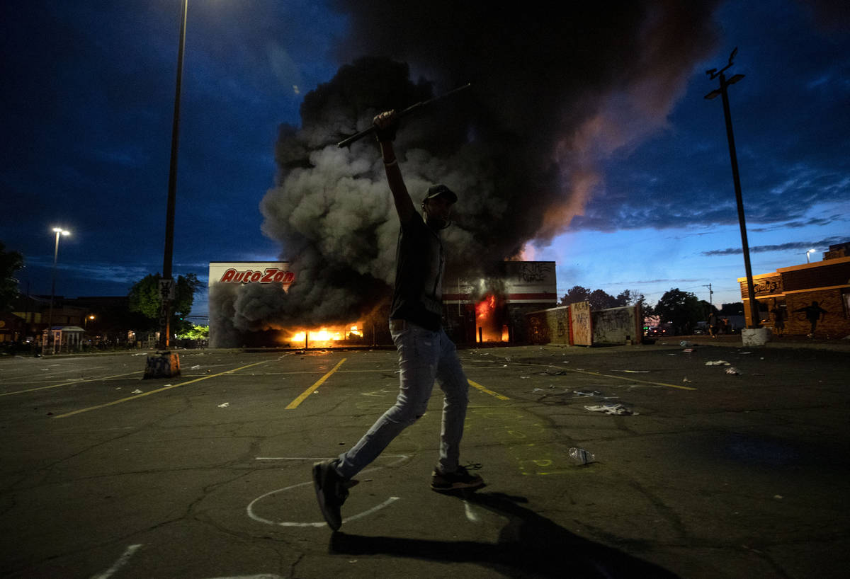 A man poses for a photo in the parking lot of an AutoZone store in flames, while protesters hol ...