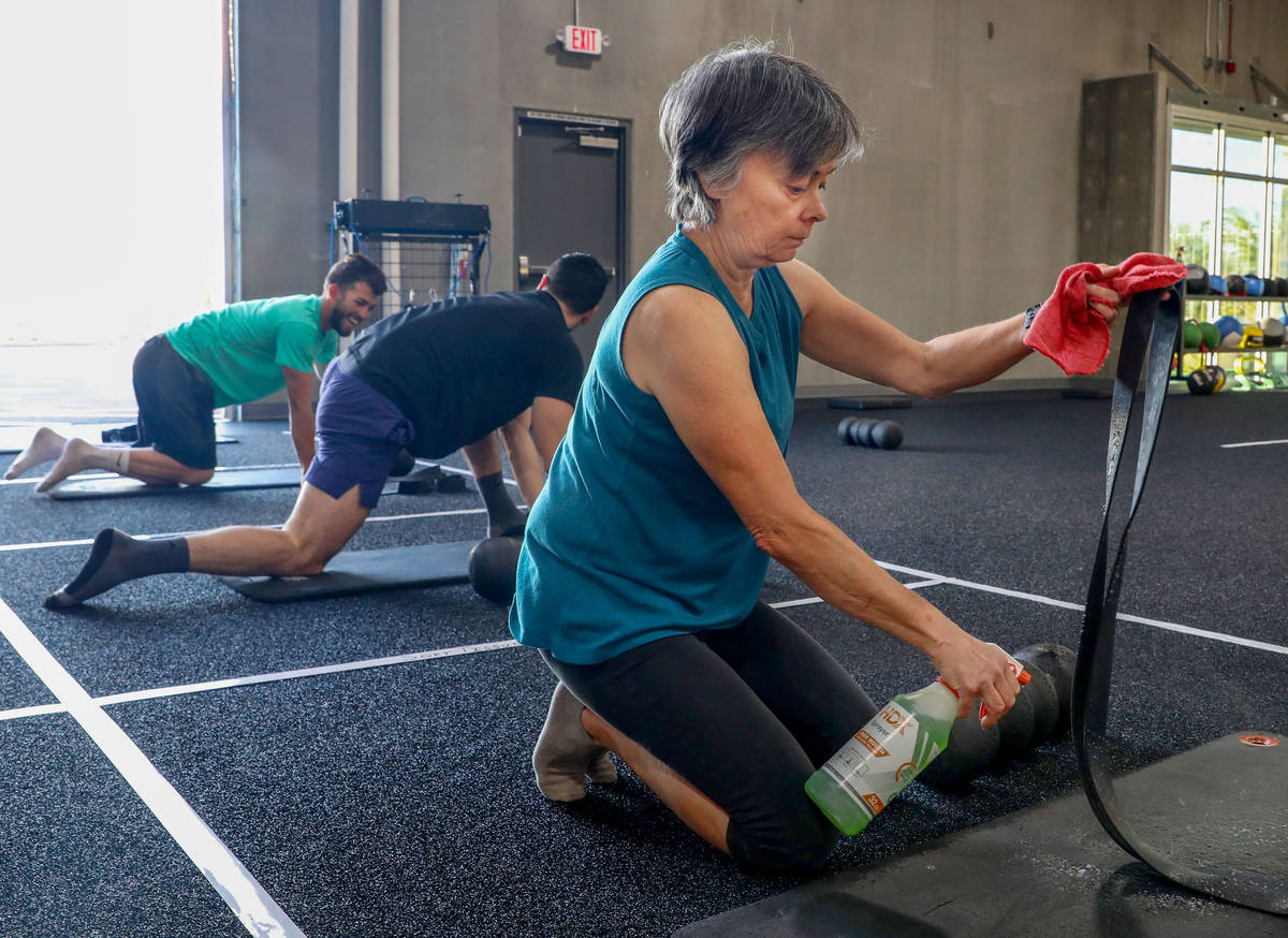 Carole Hedge, 65, member of The Gym Las Vegas, disinfects her mat and band while also following ...