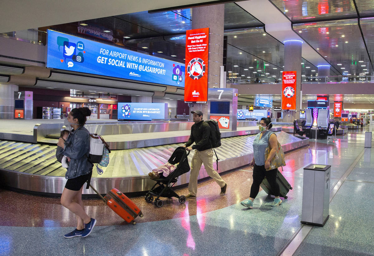 Travelers walk by new signage outlining coronavirus safety guidelines in the baggage claim area ...