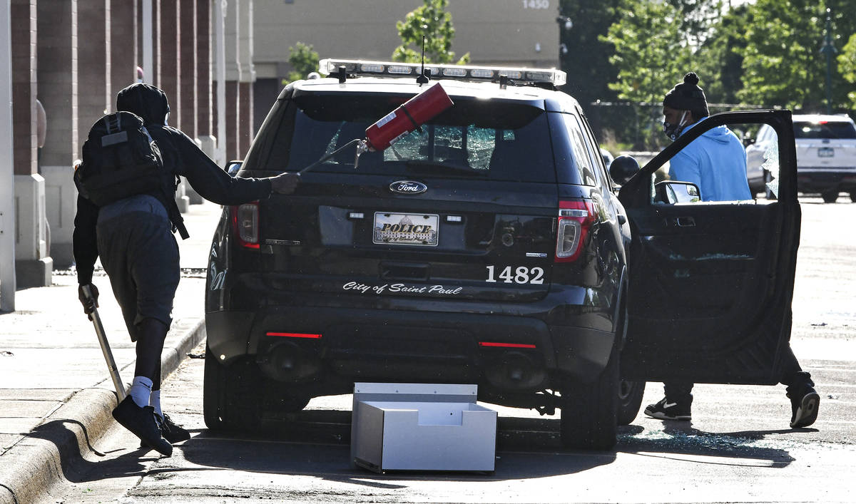 A man uses a fire extinguisher to break the rear window of a St. Paul police vehicle as another ...