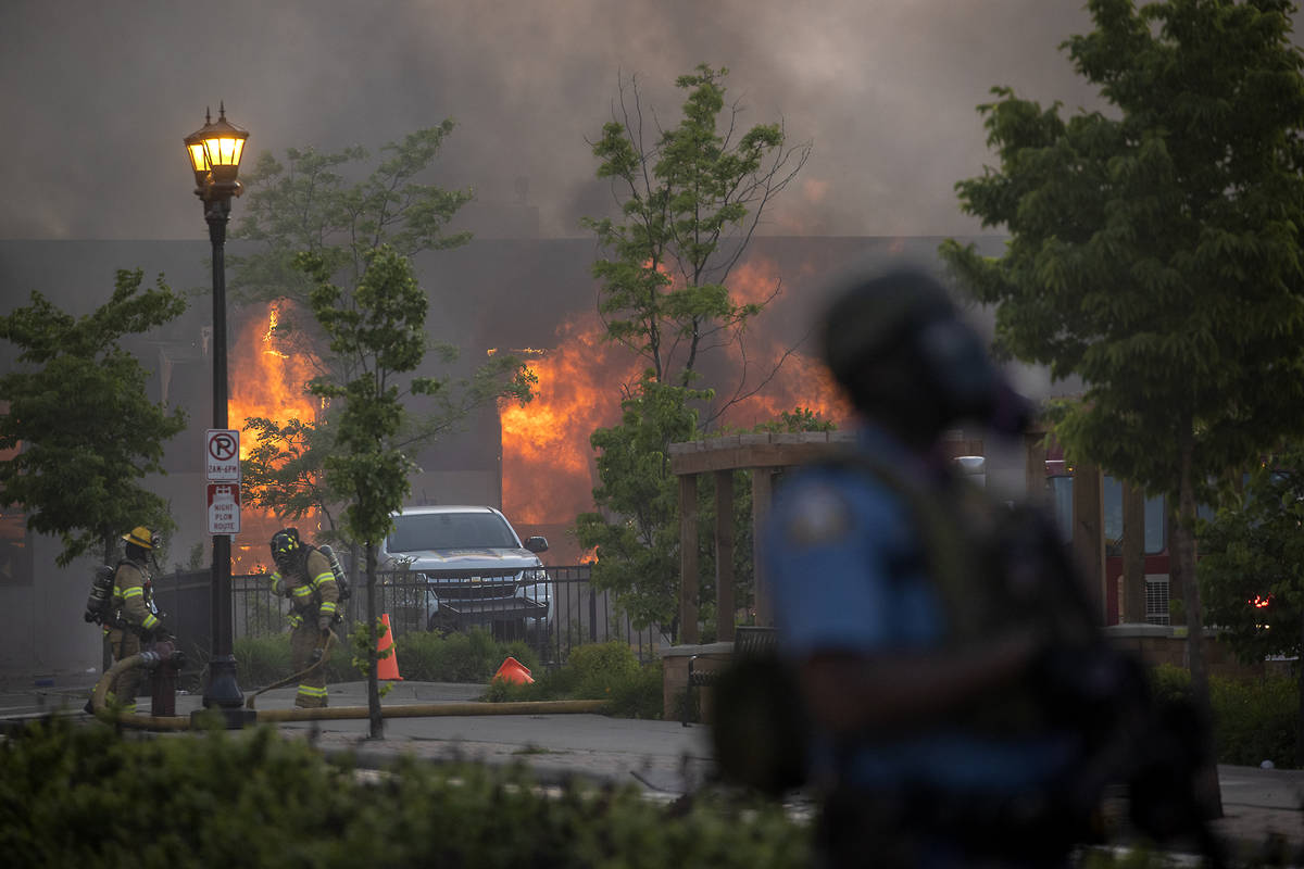 Firefighters battle flames at a business along University Avenue as riot officers police the st ...