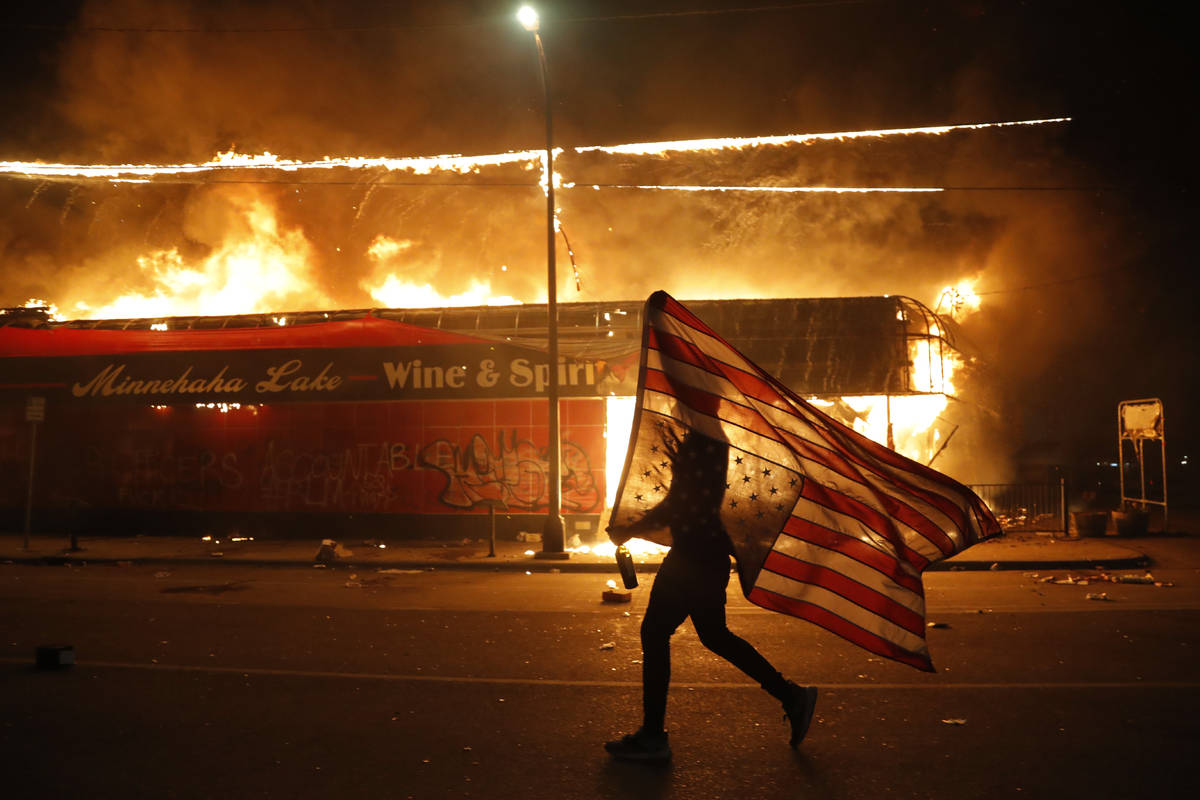 A protester carries a U.S. flag upside, a sign of distress, next to a burning building Thursday ...