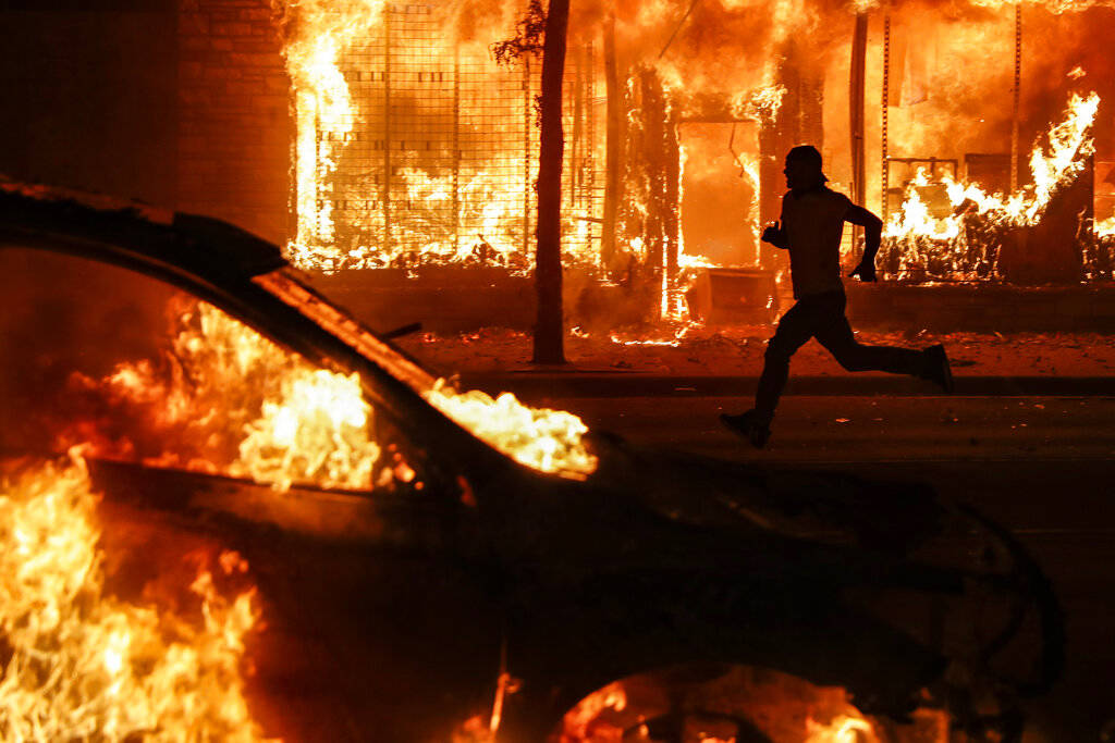 A protester runs past burning cars and buildings on Chicago Avenue, Saturday, May 30, 2020, in ...