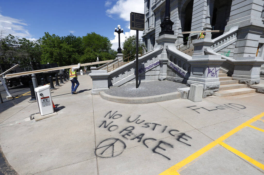 Messages that were scrawled on the sidewalk by protesters are shown as workers carry planks of ...