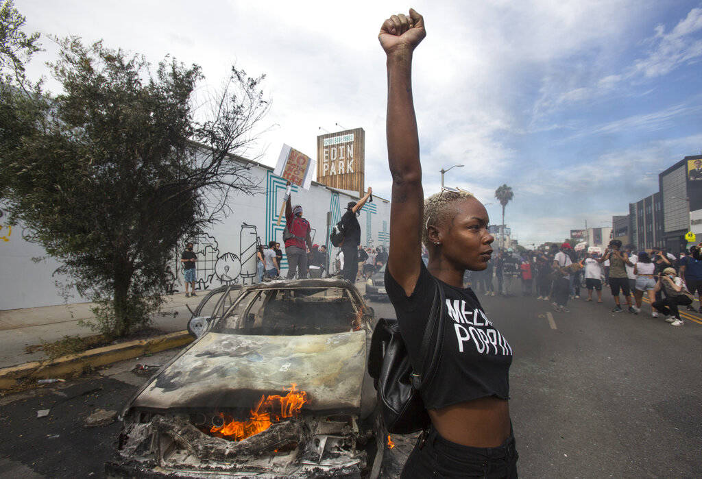A protester poses for photos next to a burning police vehicle in Los Angeles, Saturday, May 30, ...