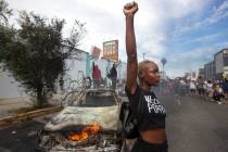 A protester poses for photos next to a burning police vehicle in Los Angeles, Saturday, May 30, ...