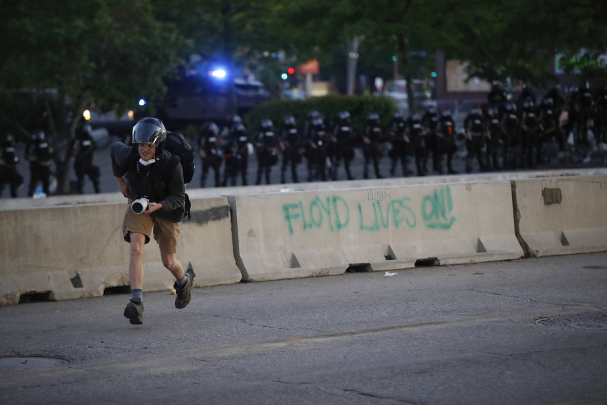 A photographer runs from a line of police in riot gear who are advancing on protesters near the ...