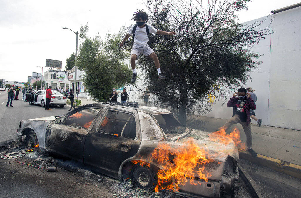 A person jumps on a burning police vehicle in Los Angeles, Saturday, May 30, 2020, during a pro ...