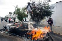 A person jumps on a burning police vehicle in Los Angeles, Saturday, May 30, 2020, during a pro ...