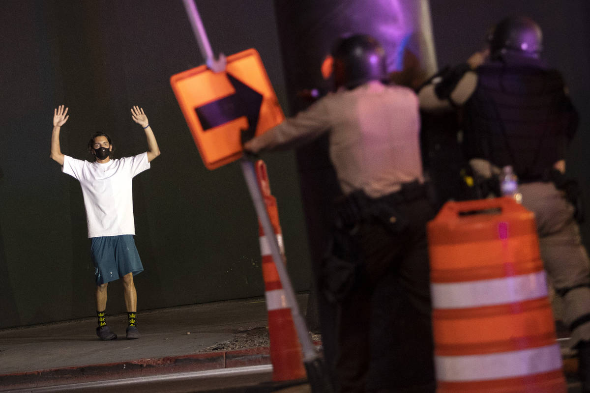 One protester puts his hands up while standing on the sidewalk as police officers ready to fire ...