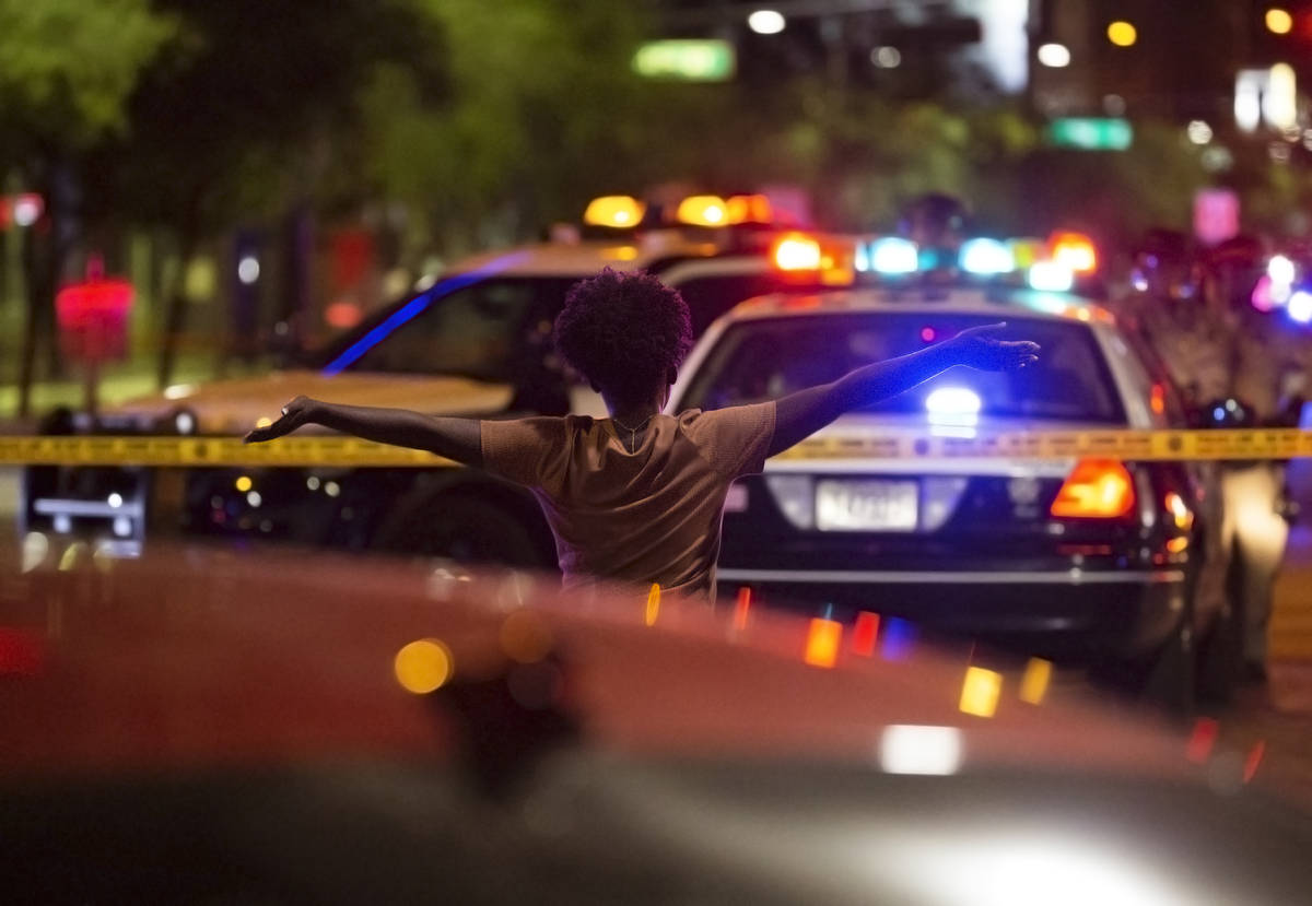 A woman walks towards police with her hands in the air after learning a protester was shot and ...