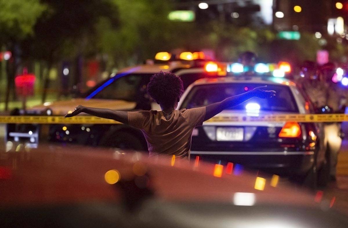 A woman walks toward police with her hands in the air after learning that a protester was shot ...