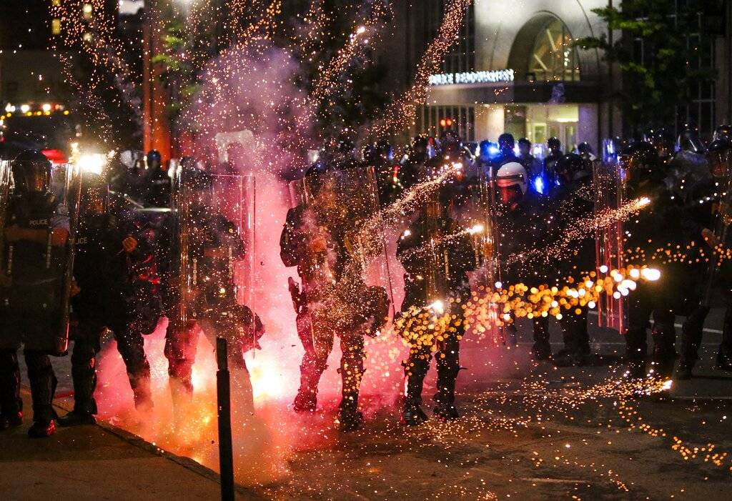 Fireworks go off in front of police, who with protesters in front of police headquarters in St. ...