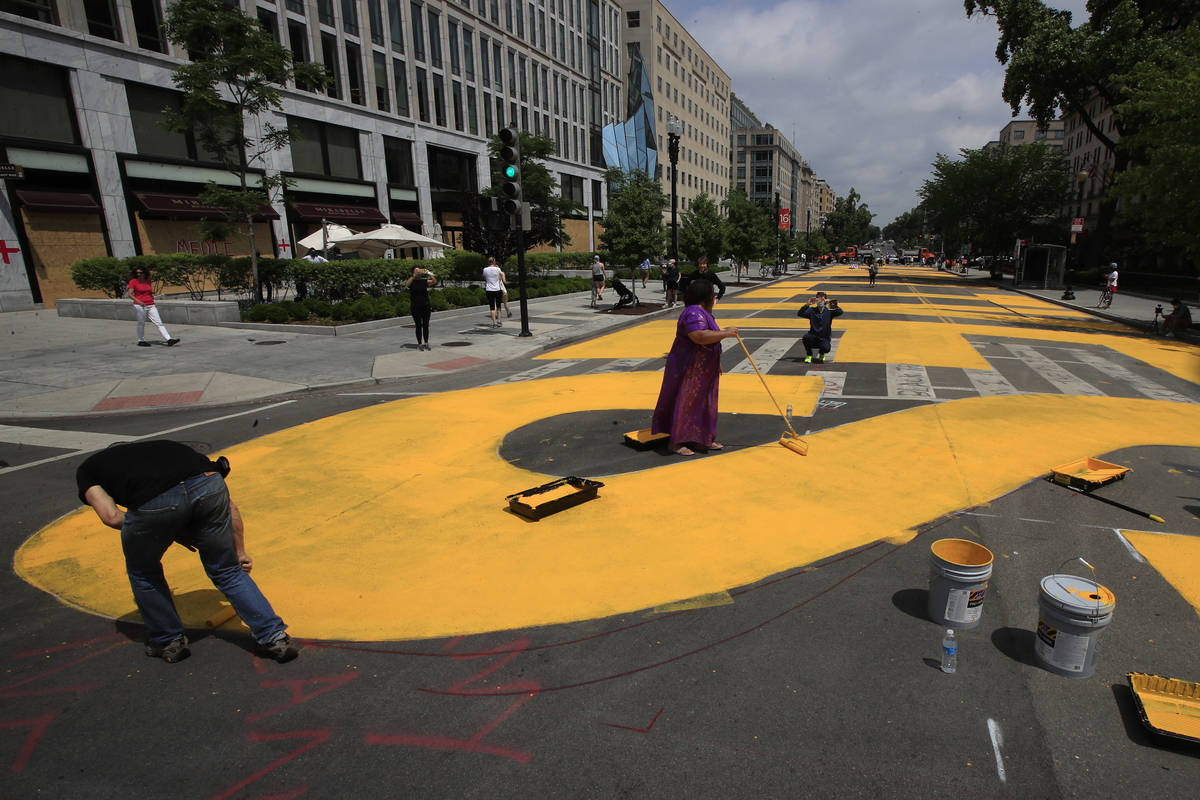 City workers and activists paint the words Black Lives Matter in enormous bright yellow letters ...