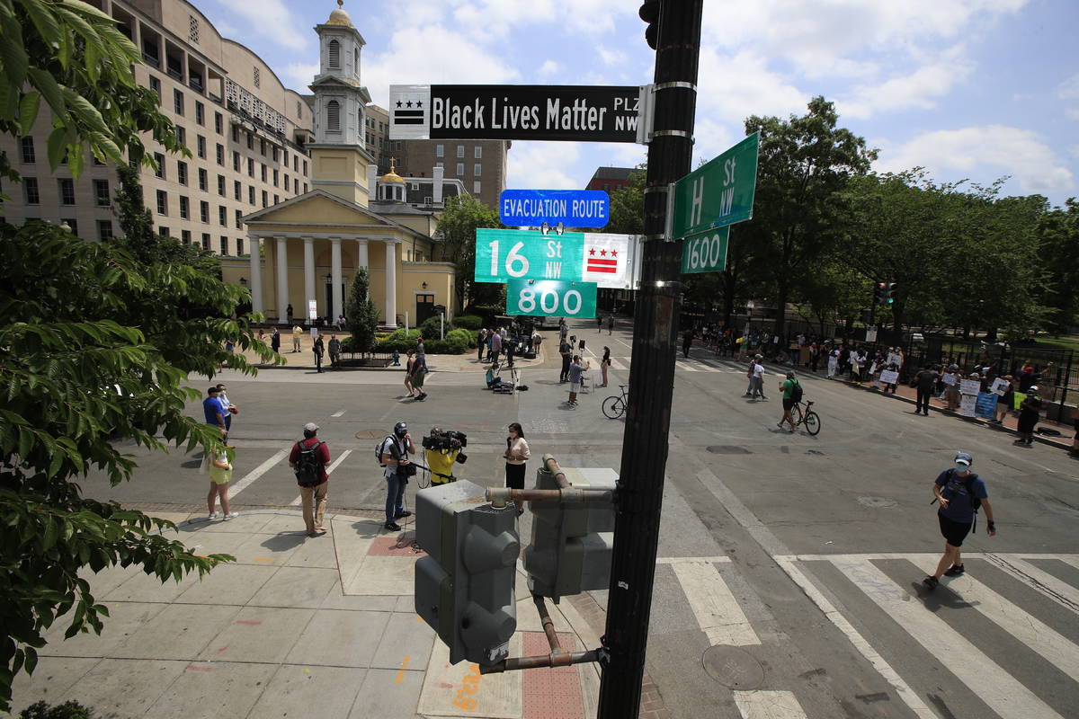 With St. John's Church in the background, people walk under a new street sign on Friday, June 5 ...