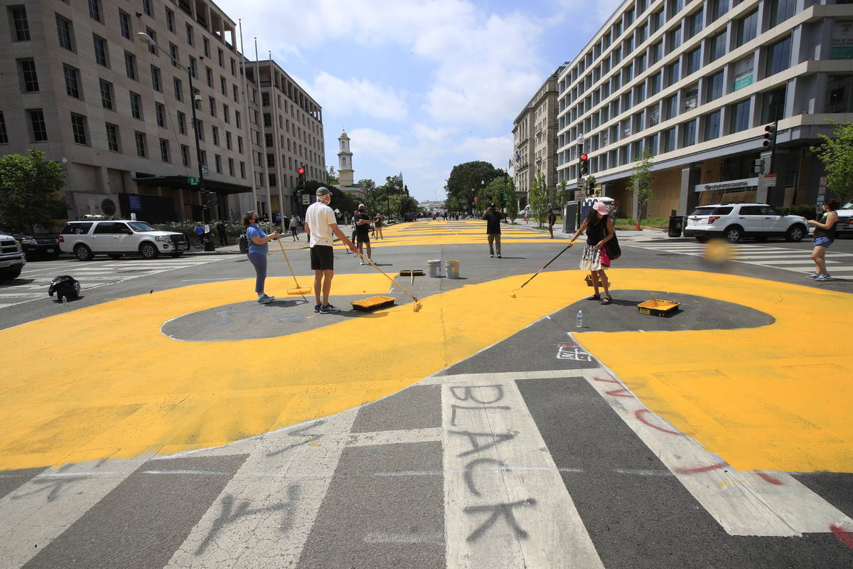 City workers and activists paint the words Black Lives Matter in enormous bright yellow letters ...
