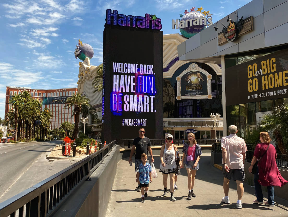 Visitors walk along the Las Vegas Strip with a sign for Harrah's advertising they are open for ...