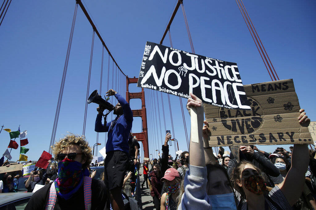 A man speaks into a megaphone while standing with others on the center divider as traffic is st ...