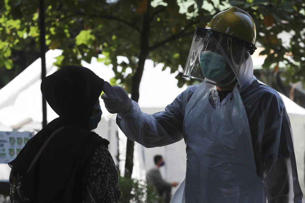 A security guard checks the body temperature of a resident at a community health center, amid c ...