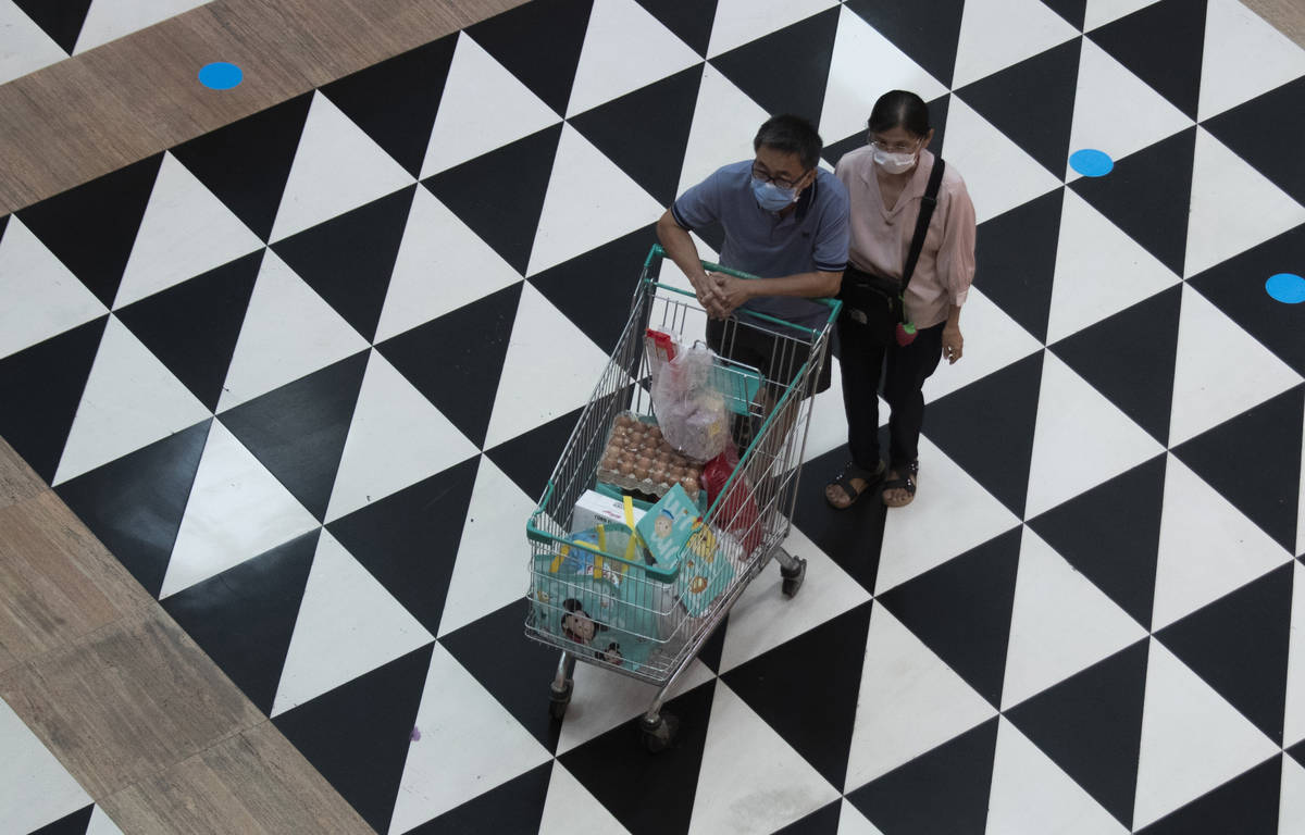 Shoppers wearing face masks to help curb the spread of the coronavirus push their shopping cart ...