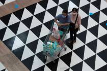Shoppers wearing face masks to help curb the spread of the coronavirus push their shopping cart ...