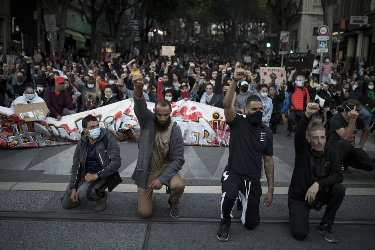 Protesters raise their fists and kneel in front of French riot police during a march against po ...