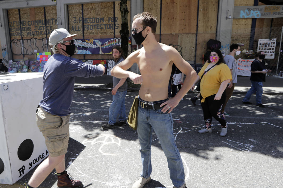 Protesters bump elbows in greeting as they work on barricades in the street adjacent to a close ...
