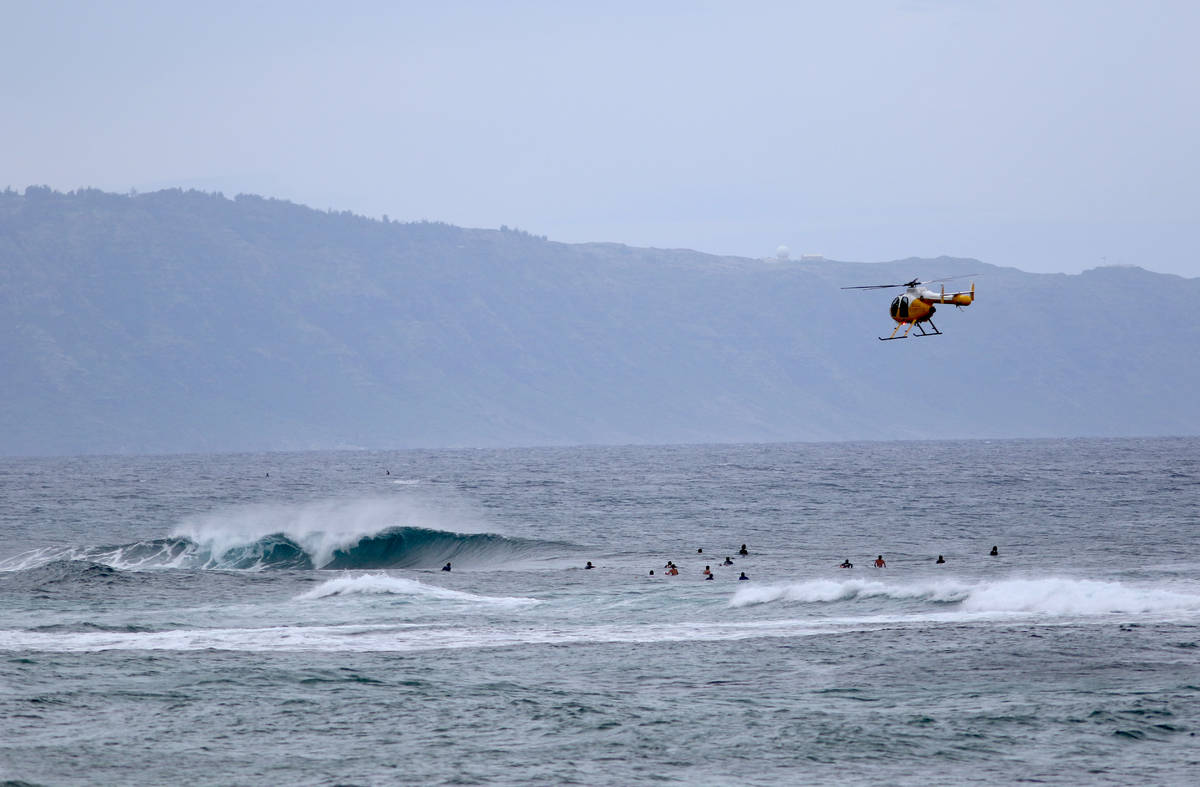 In this March 31, 2020 file photo a fire and rescue helicopter flies over a group of surfers on ...