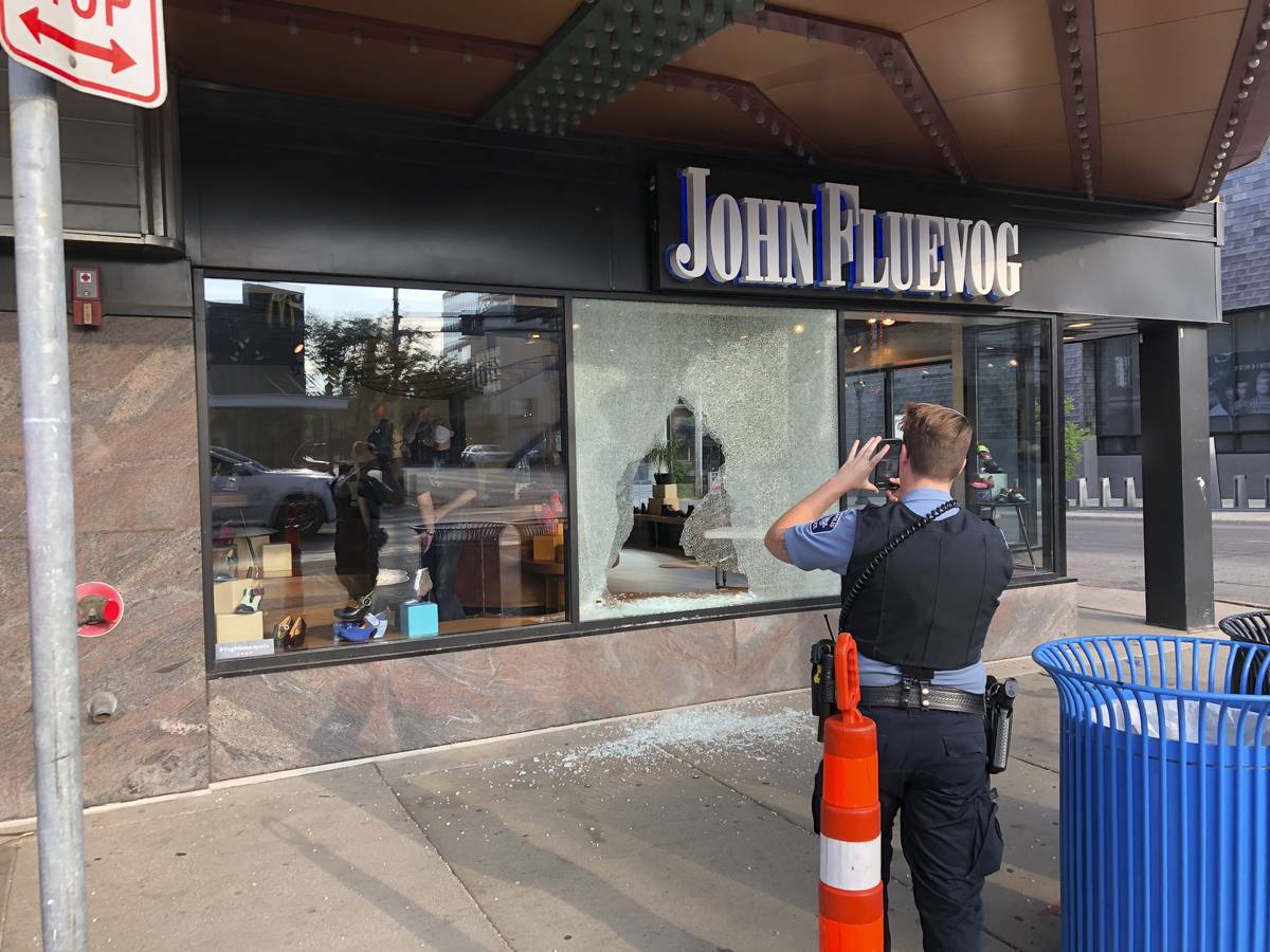 A police officer takes photos Sunday, June 21, 2020, of a shattered window of a shoe store that ...
