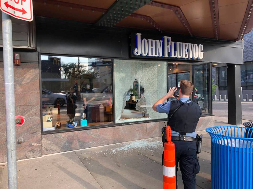 A police officer takes photos Sunday, June 21, 2020, of a shattered window of a shoe store that ...