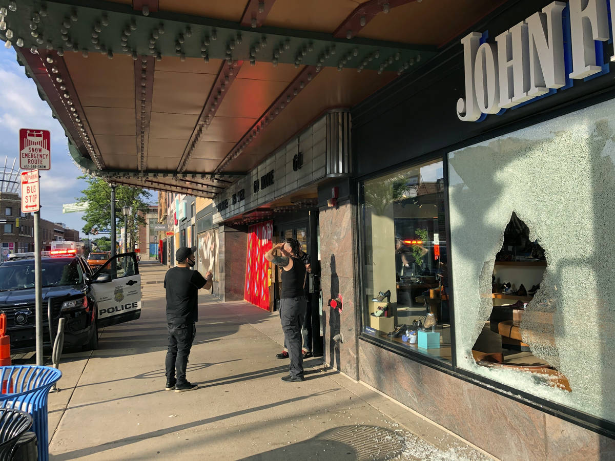 People stand near a storefront of a shoe store damaged by gunfire as a police vehicle remains o ...