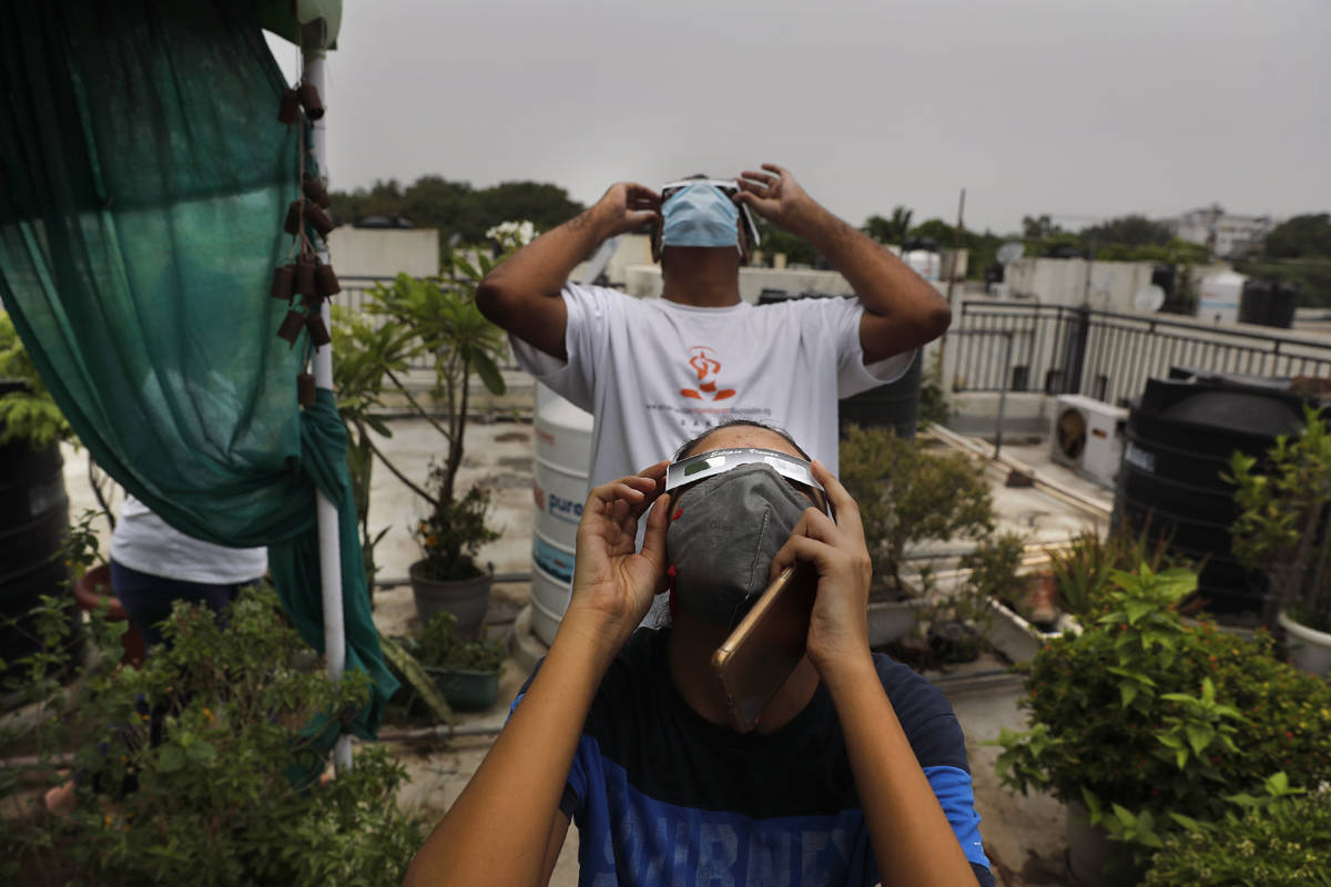 A father and his daughter watch solar eclipse from the roof of a house in New Delhi, India, Sun ...