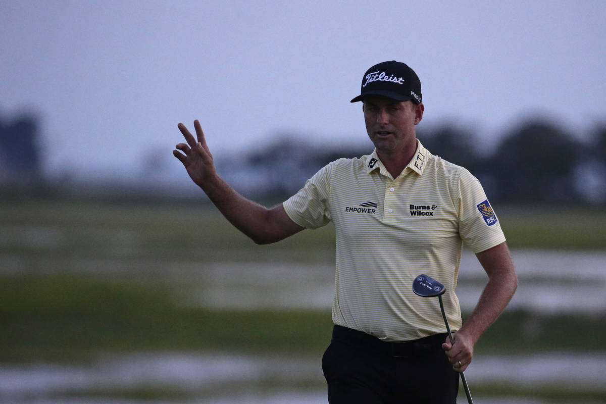 Webb Simpson waves as the sun disappears on the 18th green, on a course with no fans due to the ...