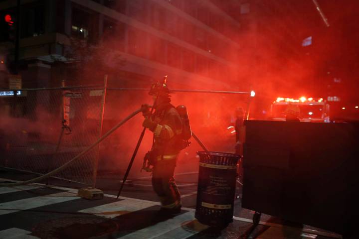 Firefighters put out a dumpster fire as protesters and police gather at Lafayette Park near the ...