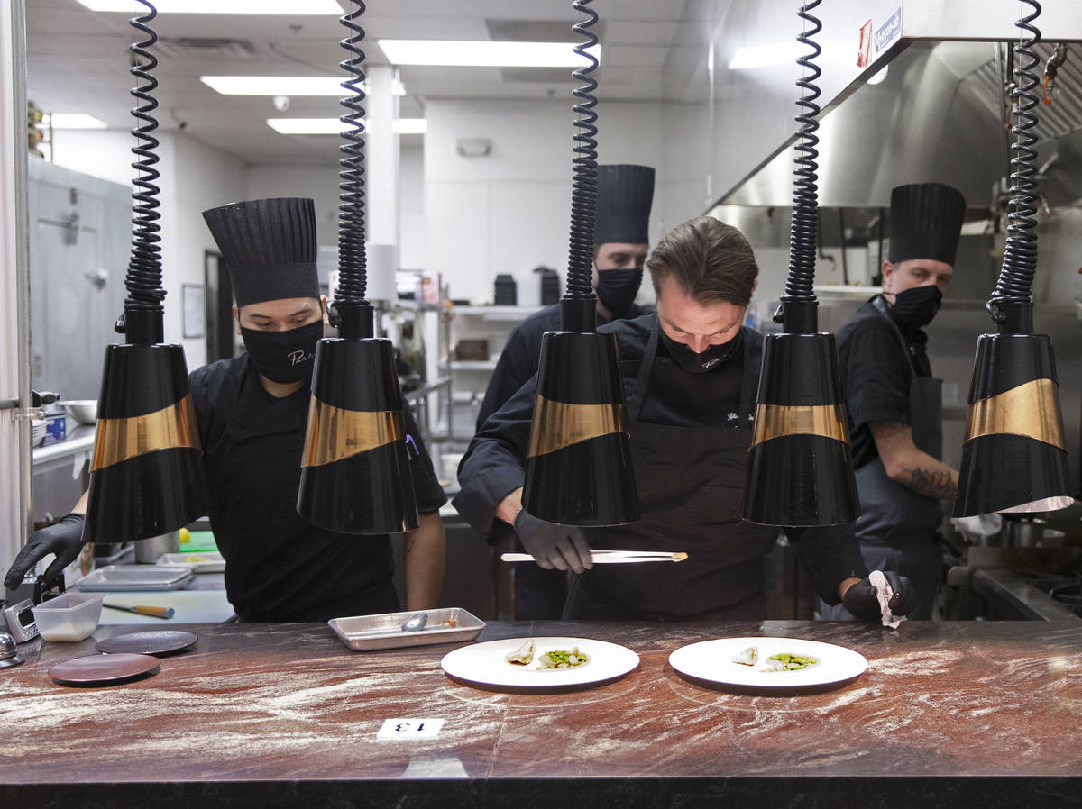 Chef Yuri Szarzewski, top/right, wears a protective mask while preparing food in the kitchen at ...