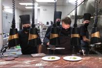 Chef Yuri Szarzewski, top/right, wears a protective mask while preparing food in the kitchen at ...