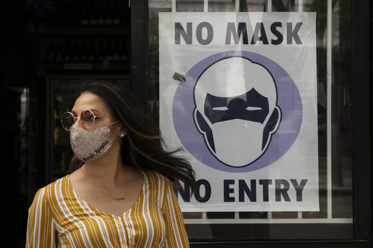 A woman walks out of a liquor store past a sign requesting its customers to wear a mask Tuesday ...