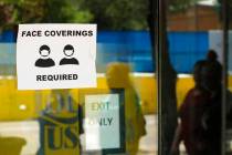 People wearing masks to protect against the spread of COVID-19 are reflected next to a sign req ...
