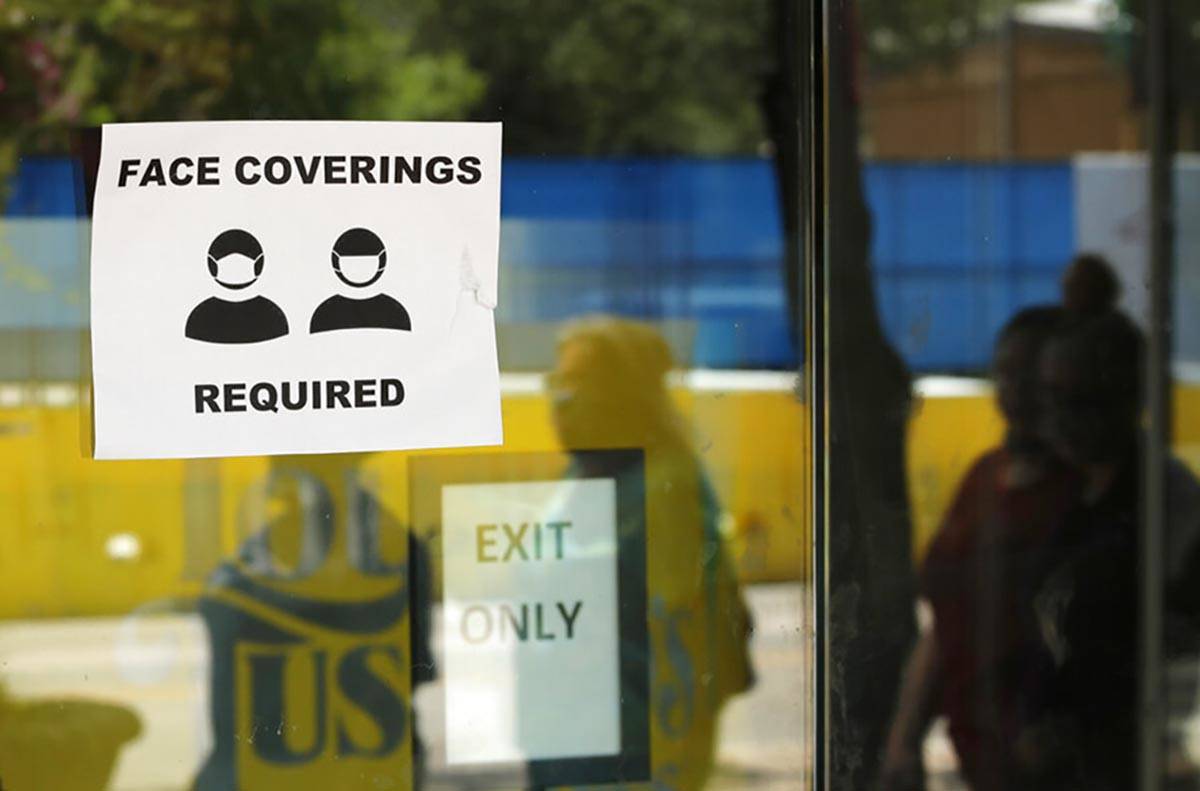 People wearing masks to protect against the spread of COVID-19 are reflected next to a sign req ...