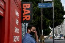 A man waits for a bus near a bar closed due to the coronavirus pandemic in Los Angeles, Monday, ...