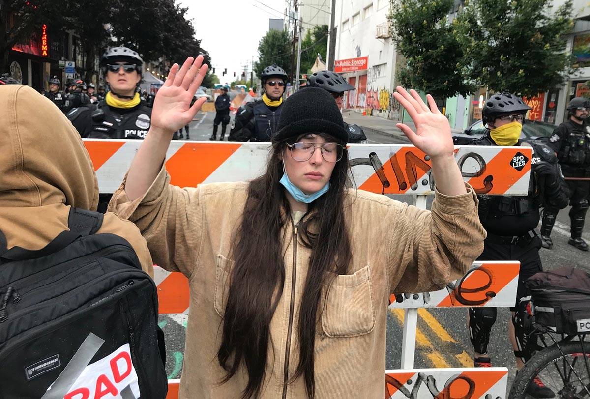 A protester stands with her hand up in front of a road blocked by Seattle police in the Capitol ...