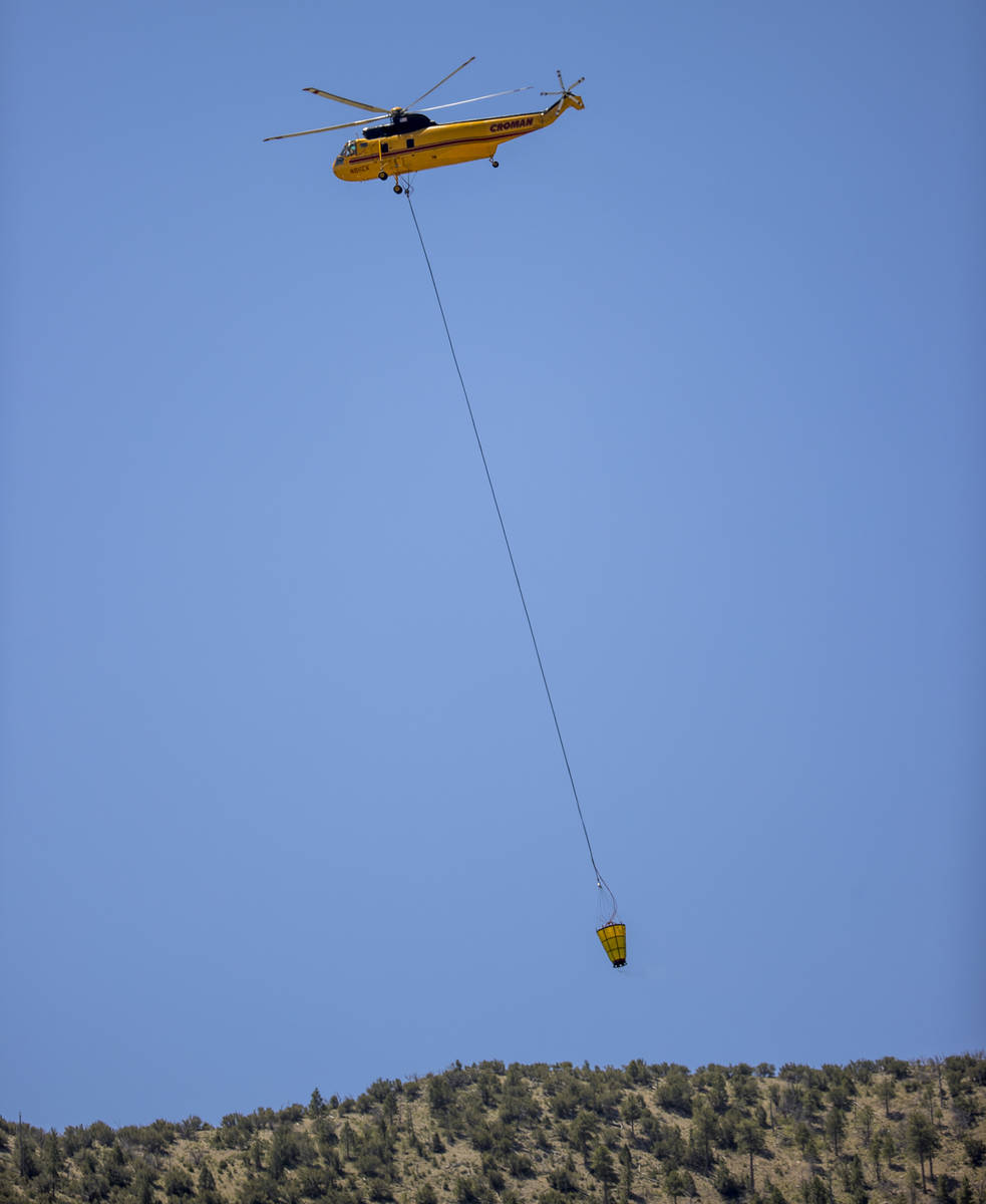 A helicopter with water bucket heads out for another drop over the Mahogany Fire on Mount Charl ...