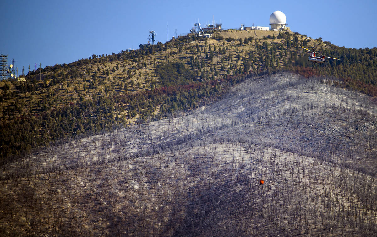 A helicopter with water bucket returns for another drop over the Mahogany Fire on Mount Charles ...