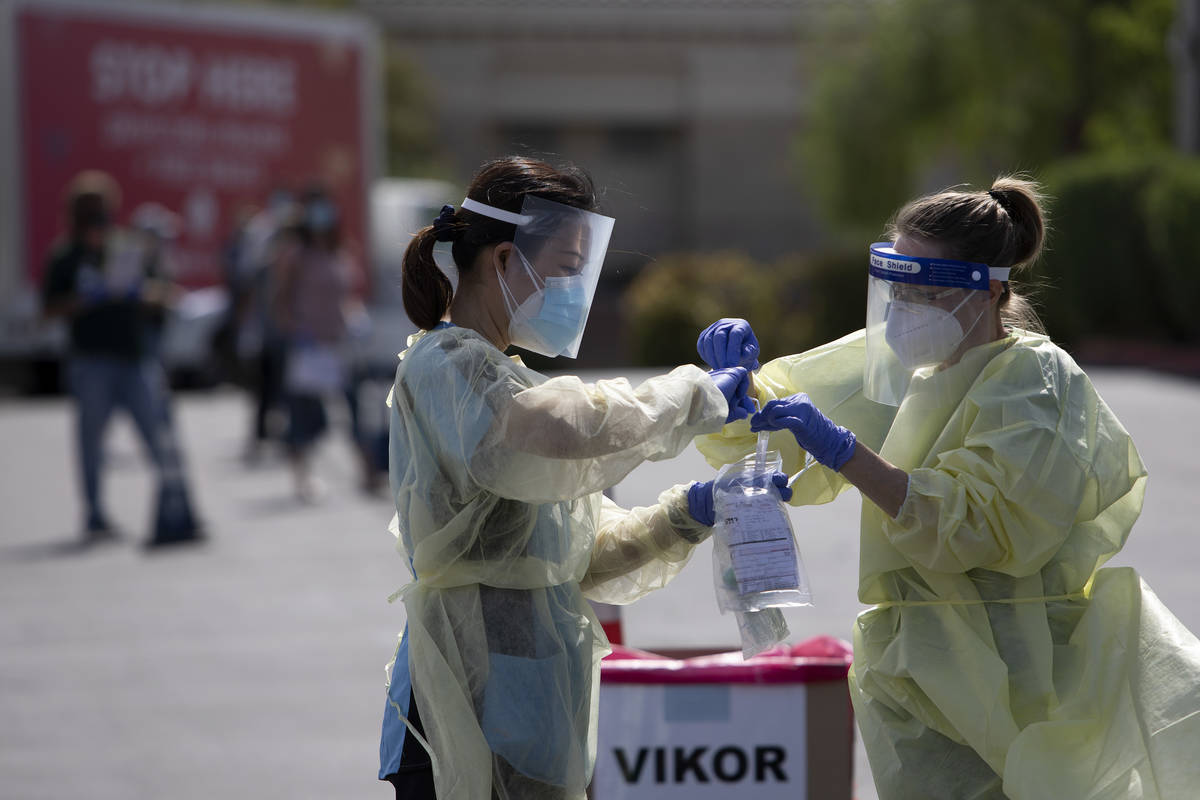 Volunteers place a nasal swab into a container at the COVID-19 drive-through testing site at Ca ...