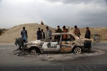 FILE - In this April 9, 2019, file photo, Afghans watch a civilian vehicle burnt after being sh ...