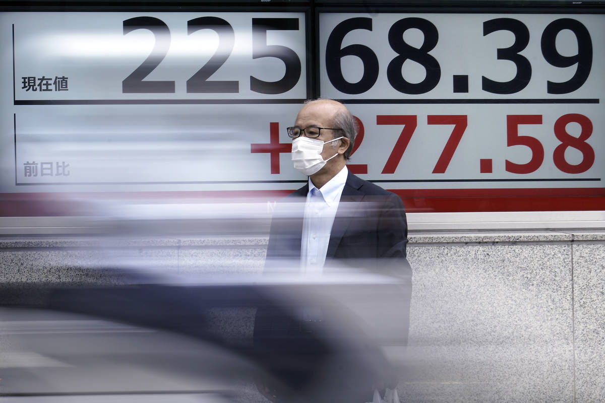 A man wearing a face mask to help curb the spread of the coronavirus stands near an electronic ...